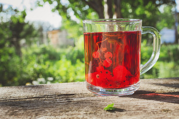 A glass beaker with berry compote stands on an old wooden table in the garden.