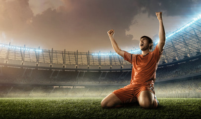 Fototapeta na wymiar soccer player in red uniform celebrates a goal on a soccer stadium holding hands above his head and screaming