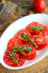 Fresh tomatoes, rucola and sesame seeds salad. Summer veggie salad on a white plate and burlap textile. Vertical photo