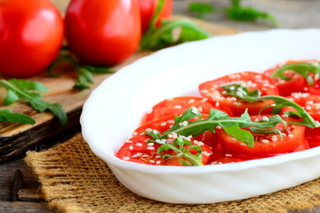 Fresh tomatoes, rucola and sesame salad. Summer vegetable salad on a white plate and burlap textile. Fresh tomatoes and rucola on a wooden table. Closeup