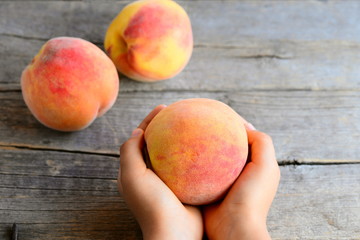 Small child holds a ripe peach in his hands. Sweet delicious peaches on an old wooden table. Encouraging healthy eating habits for kids