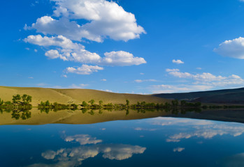 Landscape of calm lake, yellow hills and blue sky in Altai mountains. White clouds reflected in water. Chuya prairie, Altay Republic, Siberia, Russia.