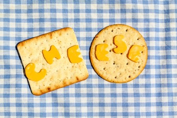 The word cheese cut out from Red Leicester cheese on crackers against ble gingham