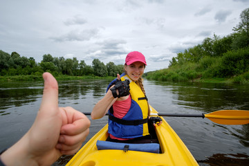 young girl in pink cap rowing in kayak over the river, showing thumb to her teammate