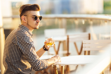 Stylish man sit on the table and drink whiskey
