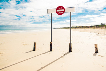 A sign do not enter, standing on the wide beach of a quiet Australian town on a sunny day.