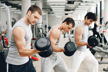 Fototapeta na wymiar Three handsome men exercising with weights in gym.