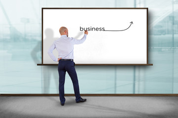 Businessman in front of a wall writing the word business with a arrow - business concept