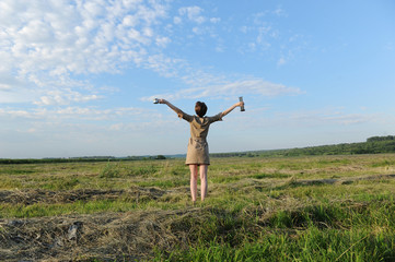 A young girl with alternative coffee brewing stands with her back against the background of summer field