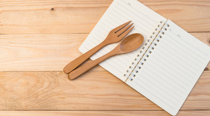 Opened blank notebook and wooden fork and spoon on wooden table