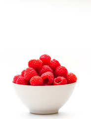 Fototapeta na wymiar A white bowlful of juicy, ripe red raspberries on an isolated white background with copy space.