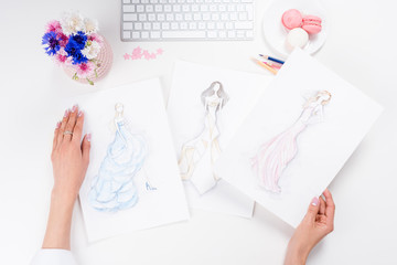 top view of female hands holding sketches of fashionable dresses at workplace