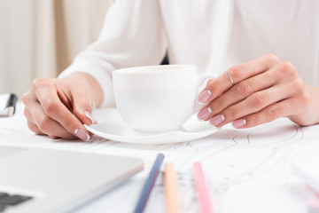 close-up view of female hands holding cup of coffee at desk