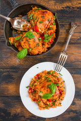 One pan tomato basil chicken and rice in a black cast-iron skillet and on a white vintage plate on the wooden rustic table, top view.
