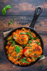 One pan tomato basil chicken and rice in a black cast-iron skillet on the wooden rustic table, top view.