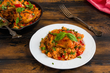 Crispy chicken thighs baked over a bed of tomato, basil and rice. Black cast-iron pan and white vintage plate on the wooden rustic table.