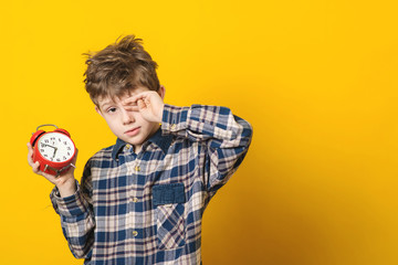 Little boy waking up with alarm clock, isolated on yellow background.