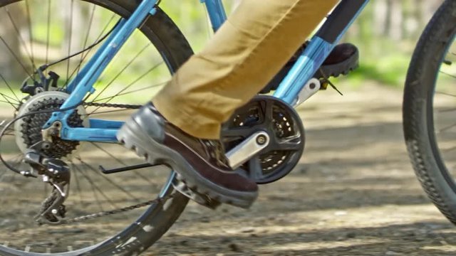 Tracking with low-section of legs of unrecognizable tourist in boots turning pedal on bicycle and riding through forest