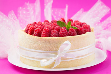 Birthday spongecake with raspberries decorated white ribbon and bow on a pink background