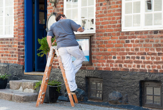 eine Malerin lackiert ein Fenster an einem historischen Gebäude