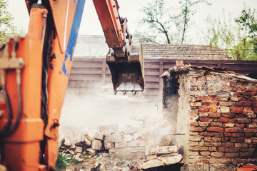 industrial close up of excavator using scoop for demolishing old house and ruins