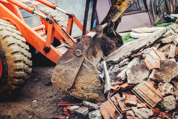 bulldozer demolishing concrete brick walls of small building and gathering debri, loading into...
