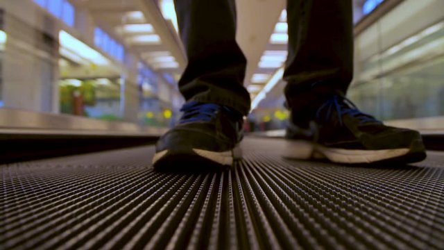 Closeup front view on man legs traveler using moving flat escalator at airport terminal