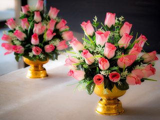 Bouquet of pink artificial flowers on gold color tray with pedestal.