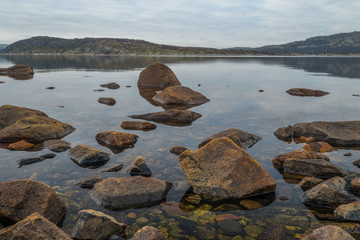 In the fall of seashore with big stones at low tide with reflection of clouds .