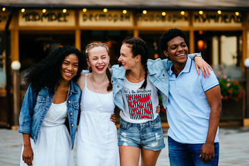 Multiethnic group of four friends hugging and enjoying the summer outdoor in th city street.