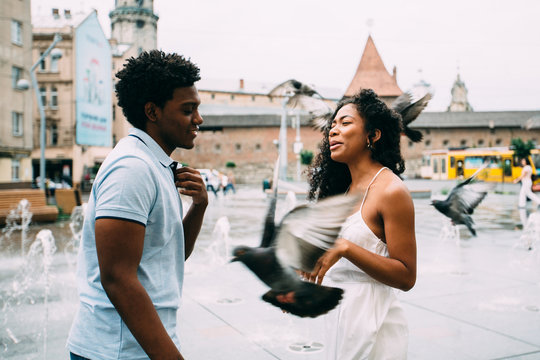 Positive emotional photo of amazing young africam american couple whirling and hugging over city square with fountain on background. Travel recreation lifestyle, water fountain.