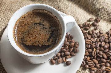 Hot cup of coffee with coffee beans on canvas.