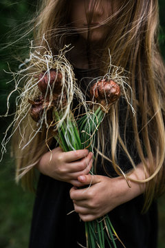 Young girl outdoors, holding bunch of fresh onion bulbs