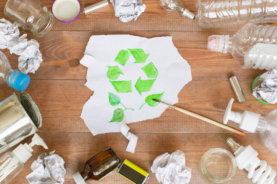 Ecology concept, a lot of recyclable objects and a drawn recycling symbol on the brown wooden background.