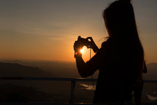 woman taking photos of sunset with mobile phone.