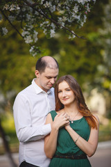 Couple in love: young girl in a long green dress and balding man in the garden. Spring or summer love story