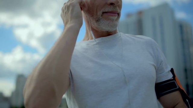 Senior positive man chosing a song for jogging