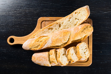 sliced French fresh bread baguette with poolish and on a wooden cutting board over dark background, flat lay