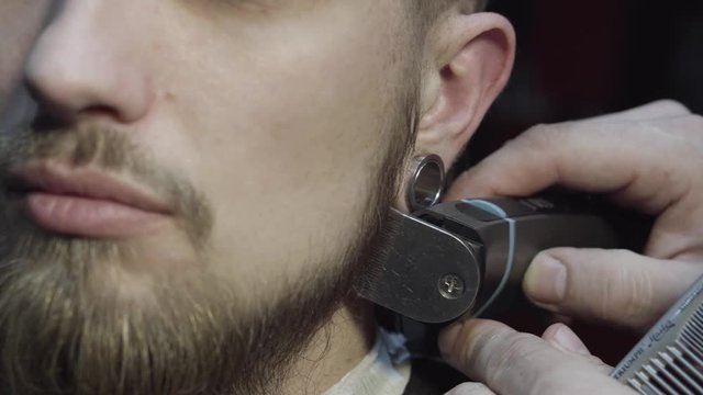 Closeup of barber cutting beard with a trimmer at a barber shop