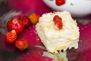 Кусок торта с маленькими ягодами клубники и крупными ягодами клубники на стеклянном подносе с рисунком в виде клубники 