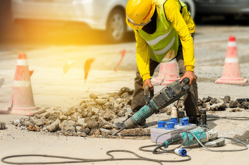 Worker drilling concrete driveway with jackhammer..Man repairing road surface with heavy duty machine,sunlight.
