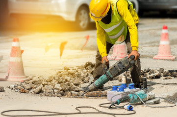 Worker drilling concrete driveway with jackhammer..Man repairing road surface with heavy duty...