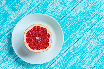 Half of grapefruit on white plate on turquoise wooden table. Healthy food and diet concept. Top view with copy space. Flat lay.