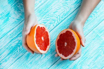 Hands holding half of grapefruit on turquoise wooden table. Healthy food and diet concept. Top view. Flat lay