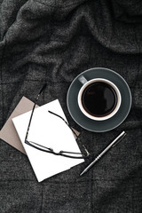 Coffee, papers and glasses on gray woolen plaid. Cozy relaxation time concept. Composition with copy space.