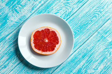 Half of grapefruit on white plate on turquoise wooden table. Healthy food and diet concept. Top view with copy space. Flat lay.