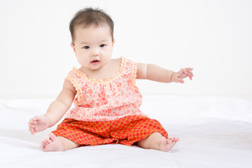 Portrait of a little adorable infant baby girl sitting on the bed and smile.