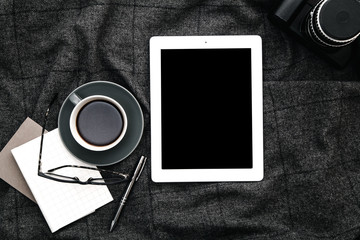 Tablet and coffee on gray woolen plaid. Vacation planning concept. Monochrome composition with text space