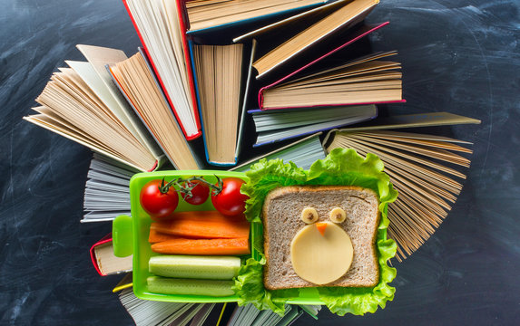 Some books with lunce box on the desk over the blackboard