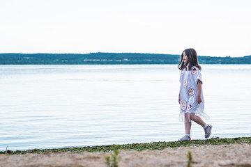 Fototapeta na wymiar Portrait of little fashionable girl walking on berth near sea